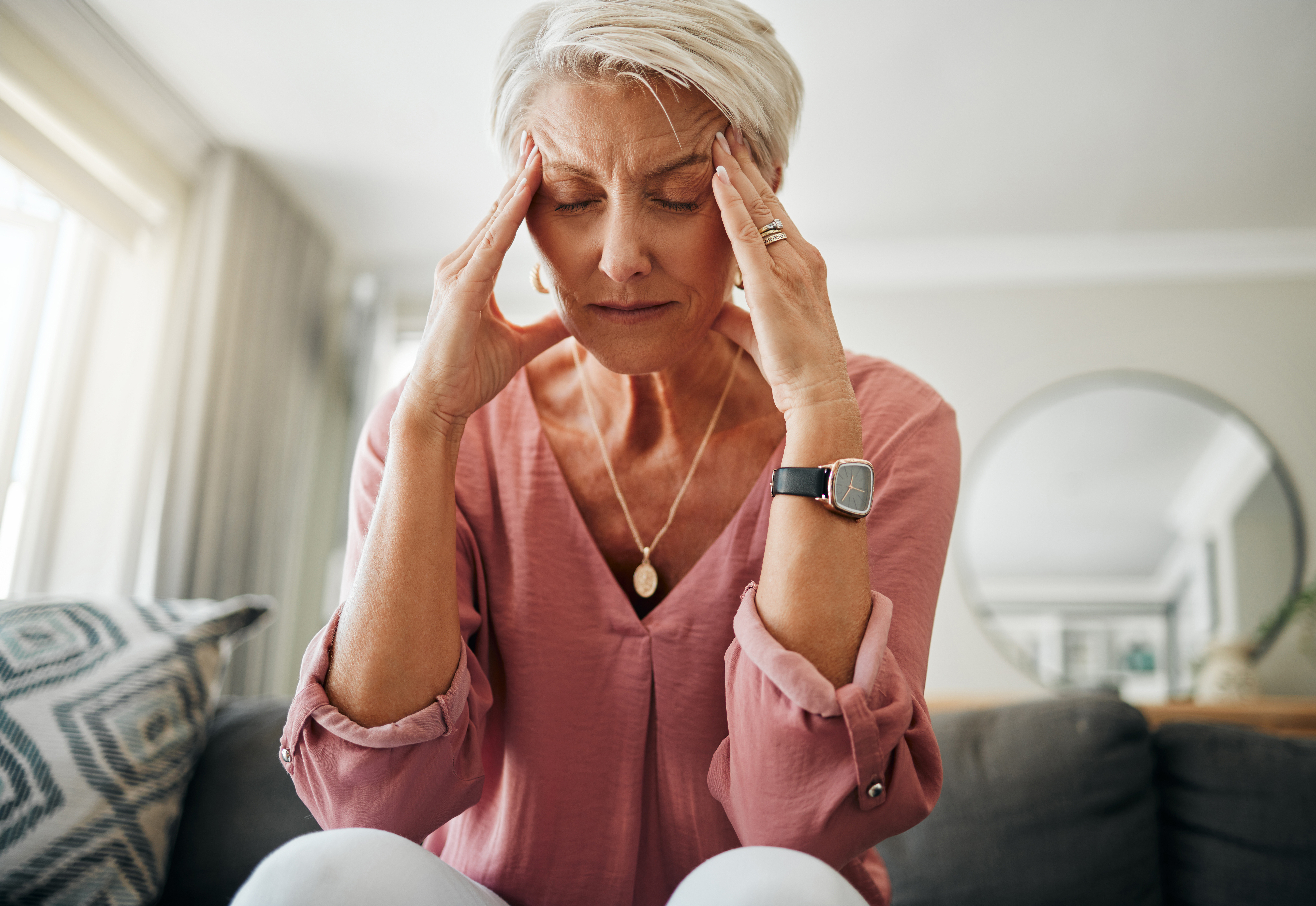 Headache pain, anxiety and senior woman thinking of mental health problem on the living room sofa in house. Sad elderly person with depression, home stress and frustrated with retirement on the couch.